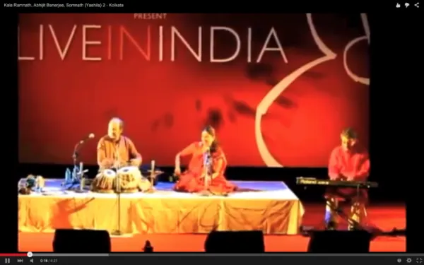 Musicians performing on stage with a red backdrop displaying 'LIVE IN INDIA'