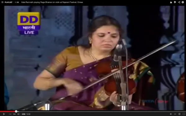 A woman wearing a traditional sari playing the violin at an event, with a microphone nearby. She appears focused on her performance.