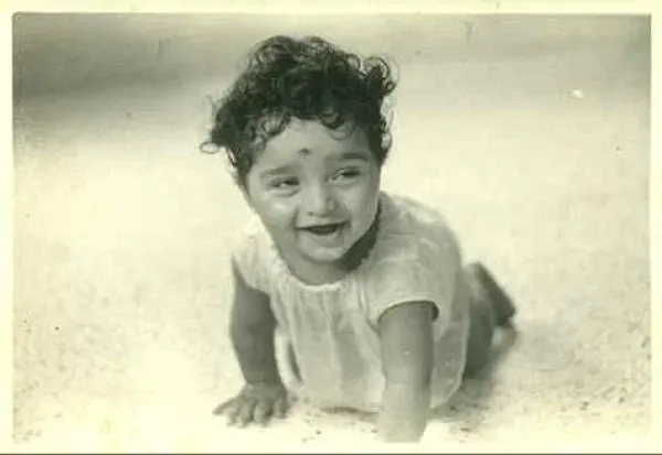 Child with curly hair smiling while crawling on the floor in a vintage black-and-white photo.