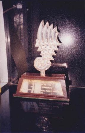 A tall trophy with a stylized hand of five fingers, each with a pointed end, mounted on a base with an inscription plaque.