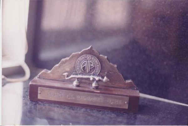 Close-up of a wooden nameplate holder with a metal emblem and a space for a name, placed on a dark surface near a window.