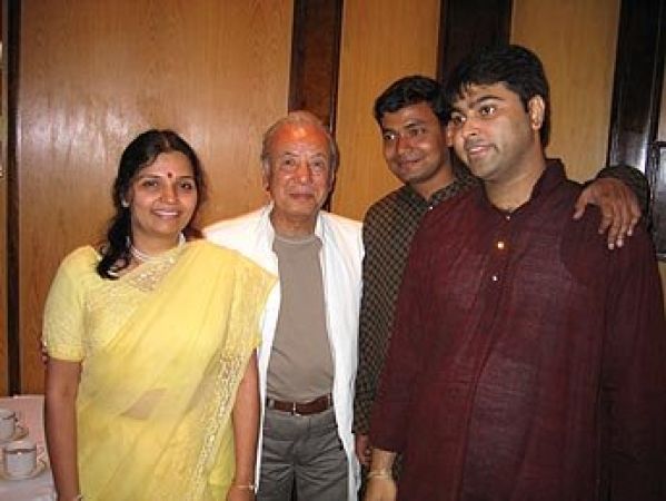 Four people, two women and two men, smiling and standing close together indoors.